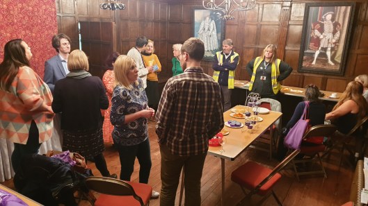 Attendees at the event standing around chatting in a wood-panelled historic room at Hall Place